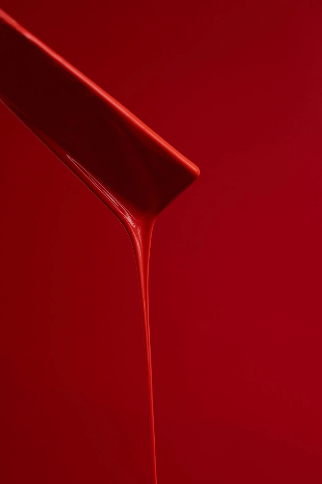 Red paint flows from the end of a mixing tool against a red background.