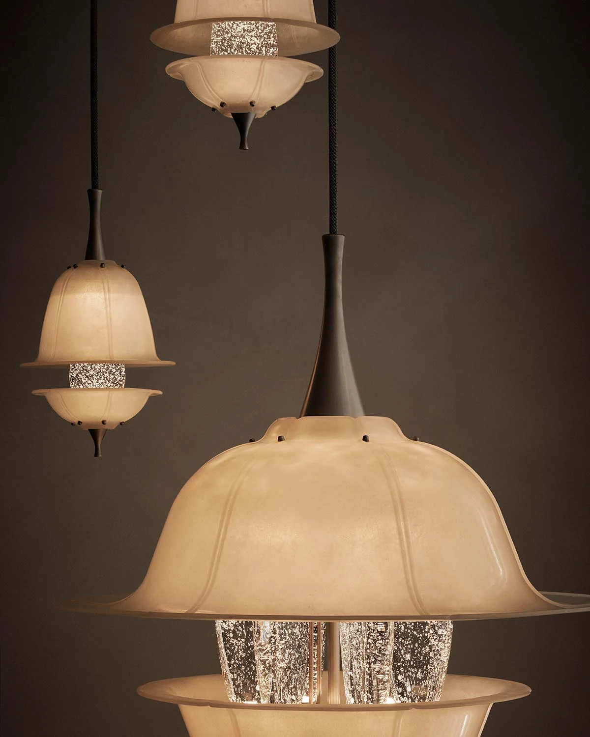 Three illuminated GOL pendants have softly curved translucent shades surrounding textured glass centres.