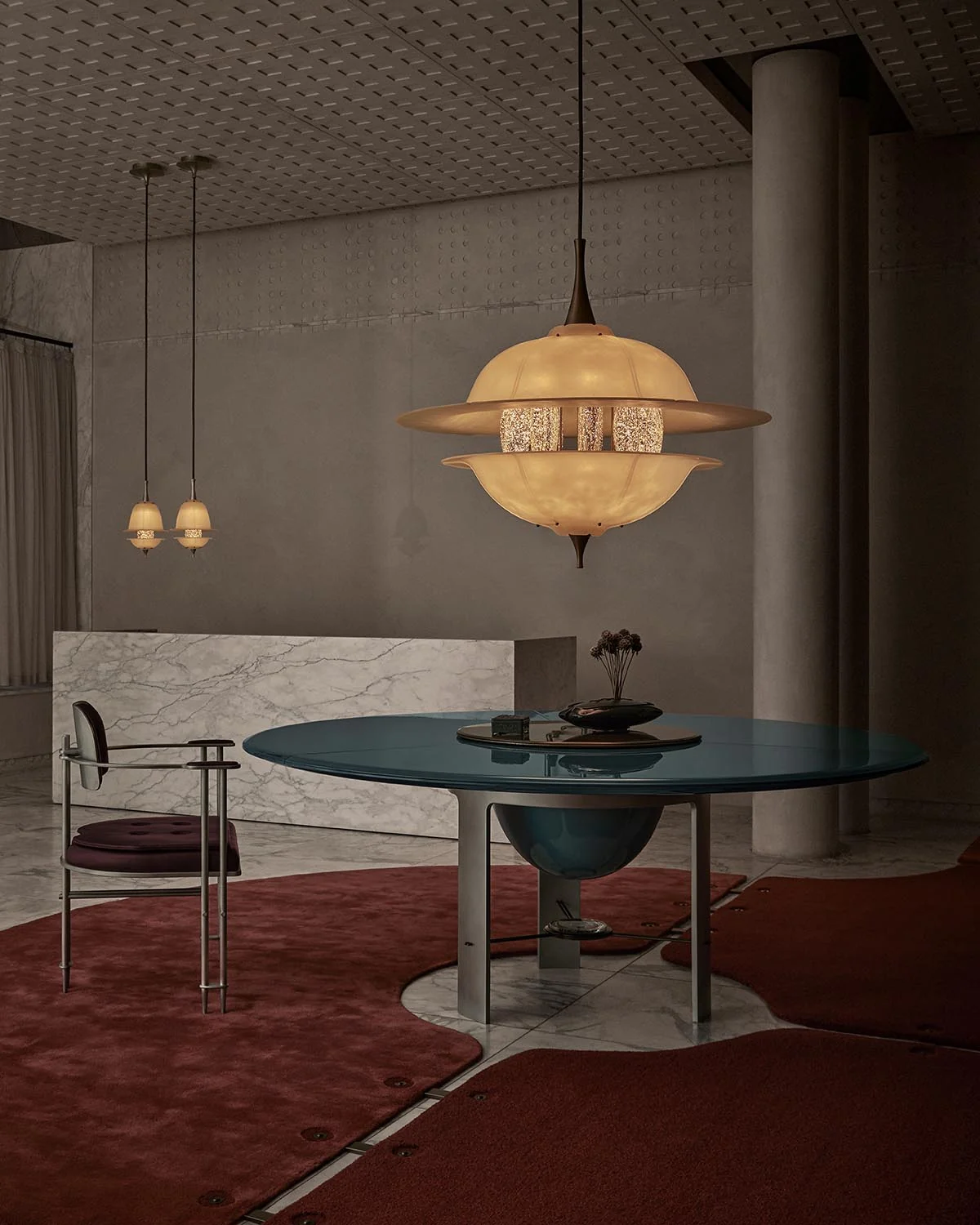 A glowing sculptural pendant hangs above a dark teal circular table in APPARATUS’s London gallery, with red rugs and pale stone surfaces.