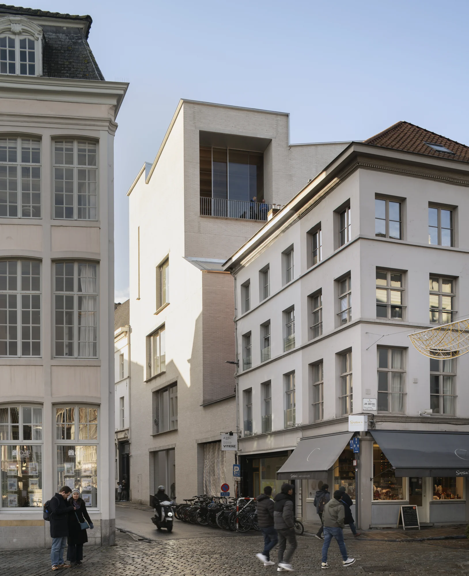 Design Museum Gent’s pale brick extension rising between historic buildings, viewed from the Grasbrug.