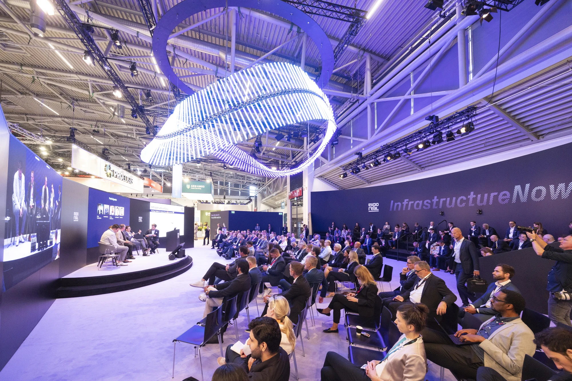 Panel speakers and a seated audience in the InfrastructureNow forum at EXPO REAL 2026.