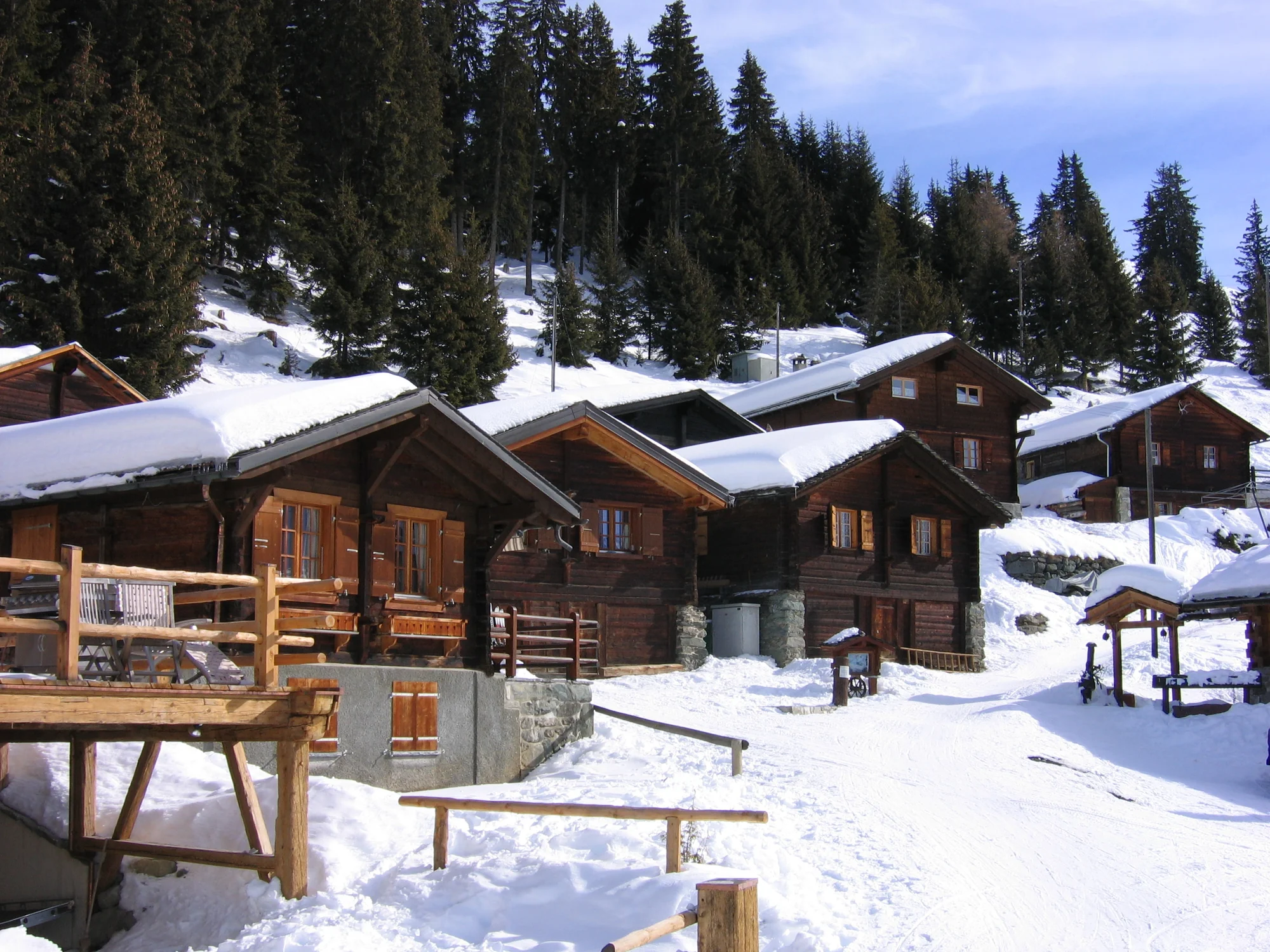 Snow-covered timber chalets below a forested slope in Verbier, Switzerland.